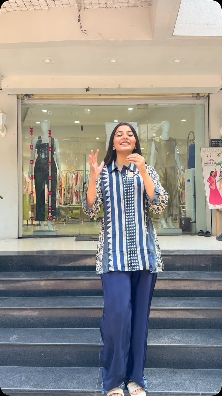 A woman in a blue patterned tunic and navy wide-leg trousers posing in front of a shop.