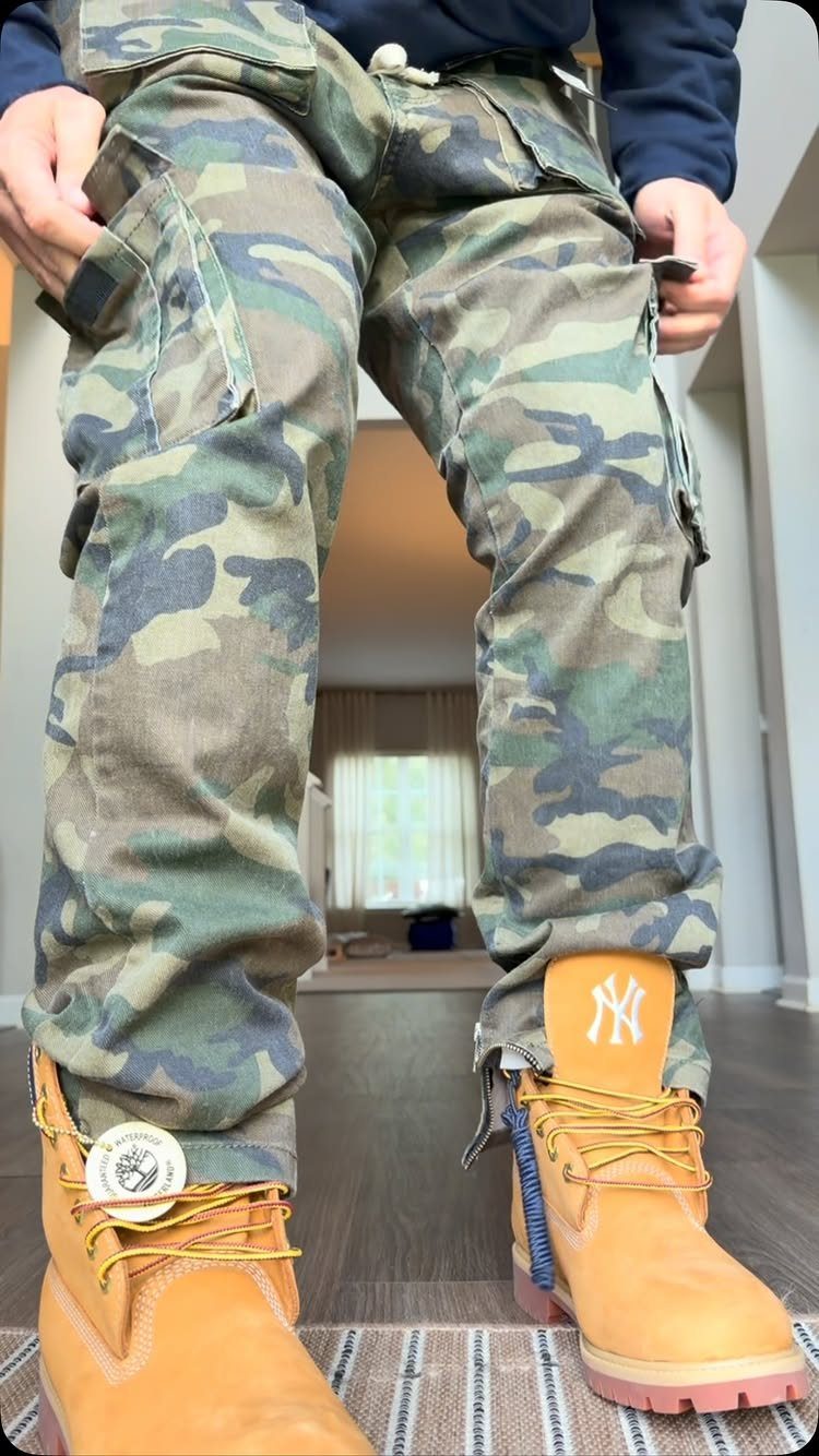 Person wearing camouflage cargo pants and tan Timberland boots standing on a wooden floor.