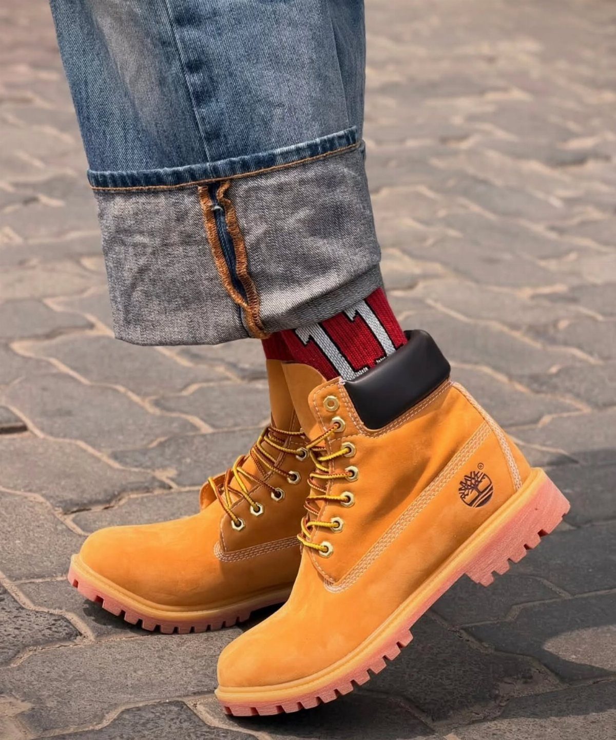 Person wearing tan Timberland boots with cuffed blue denim jeans and red patterned socks.