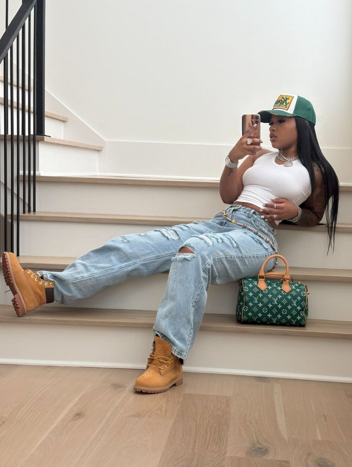 Woman in white crop top and ripped jeans sitting on stairs wearing tan boots.