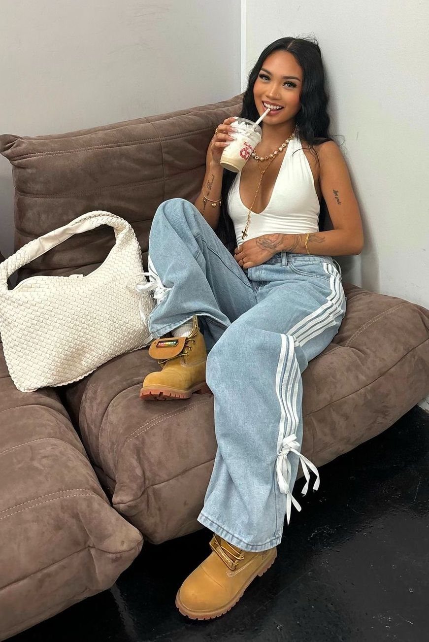 A woman in light blue striped denim pants and tan Timberland boots sitting on a sofa.