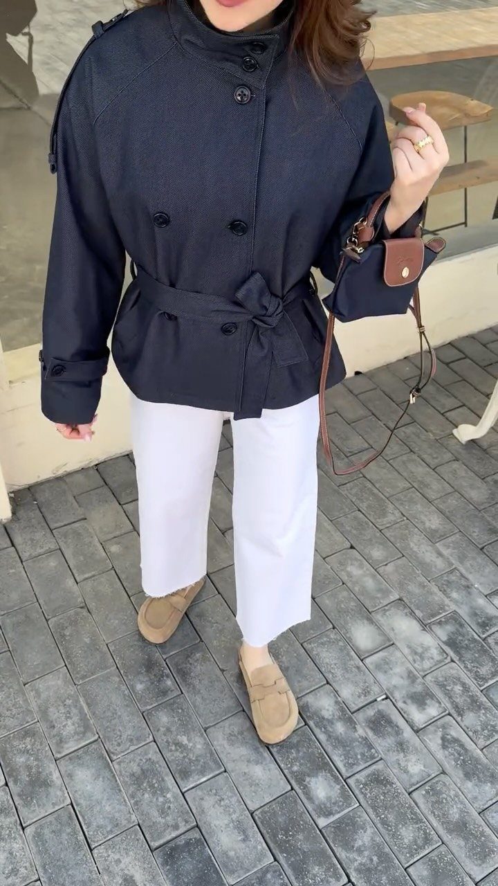 Person wearing a dark navy belted coat with white trousers and tan loafers outdoors.