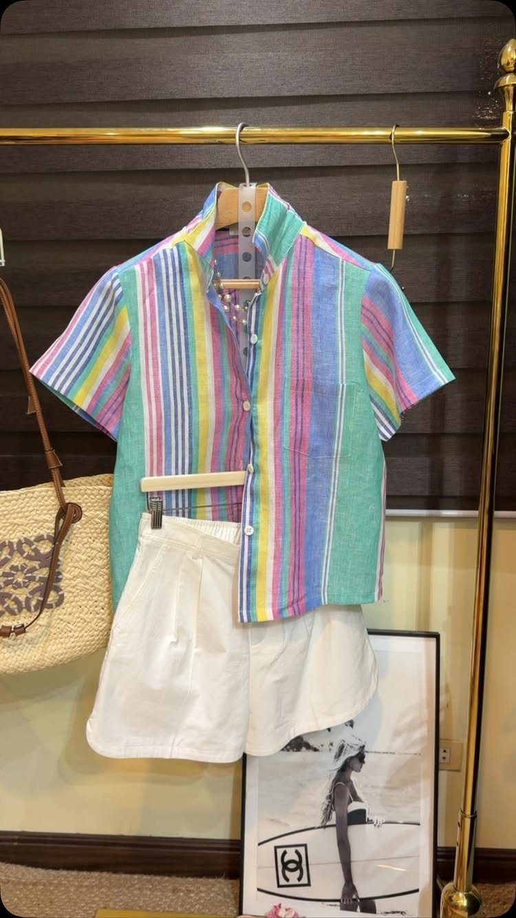 A colorful striped short-sleeved shirt hanging above a pair of white shorts on a gold rack.