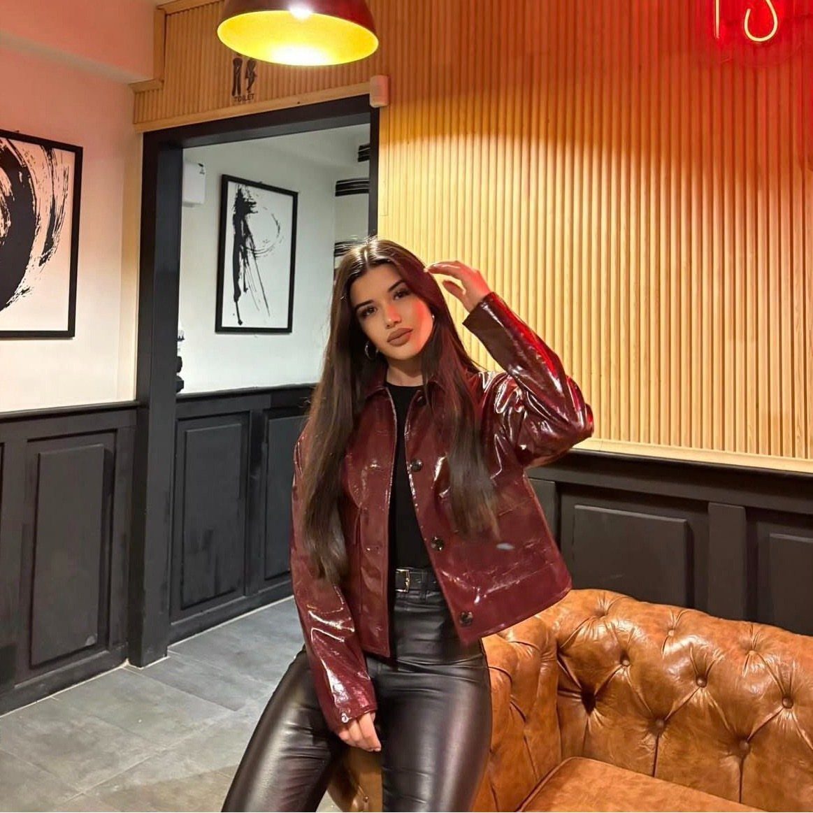 Woman posing in a burgundy jacket and black faux leather pants in a lounge.