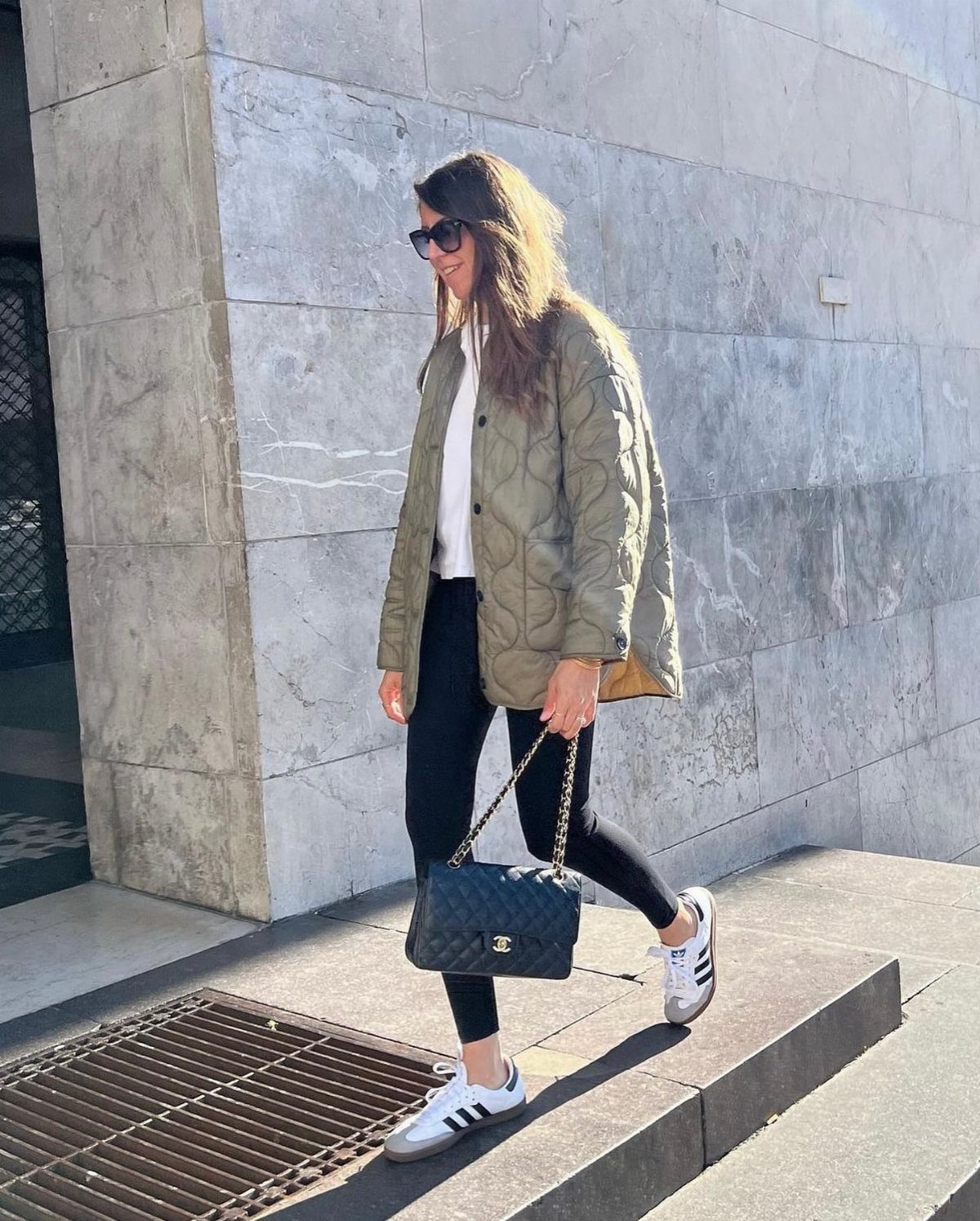 Woman walking in an olive green quilted jacket, black leggings, and white sneakers.