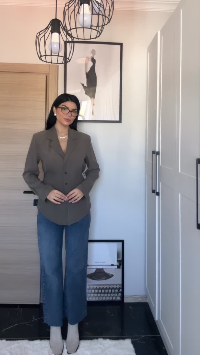 Woman posing in a grey blazer paired with blue wide-leg denim jeans and light boots.