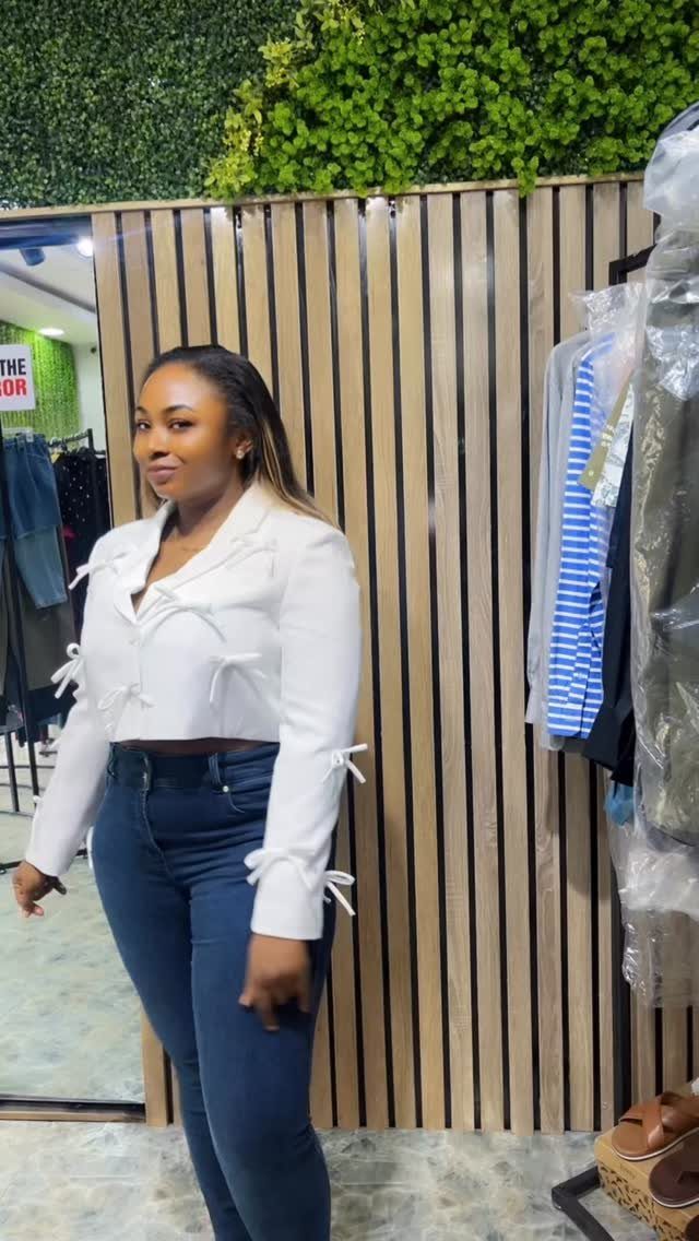 Woman posing in a white cropped blazer with tie details and dark blue jeans.
