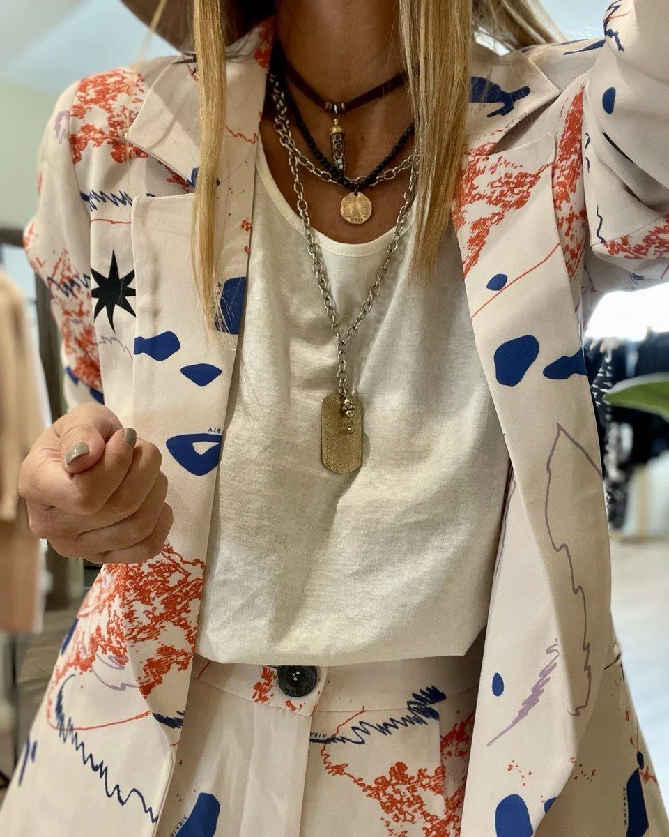 A person wearing a white blazer featuring blue and orange abstract patterns over a white t-shirt.