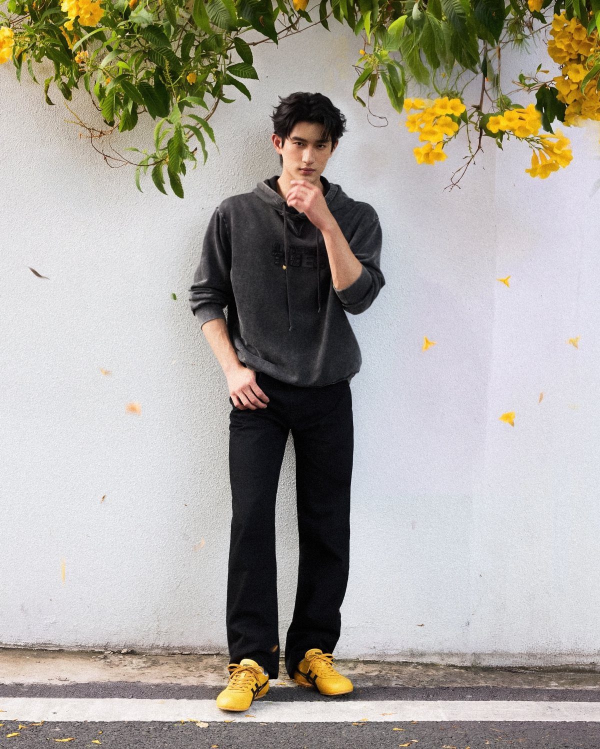 A man in a dark hoodie and black pants wearing bright yellow sneakers.
