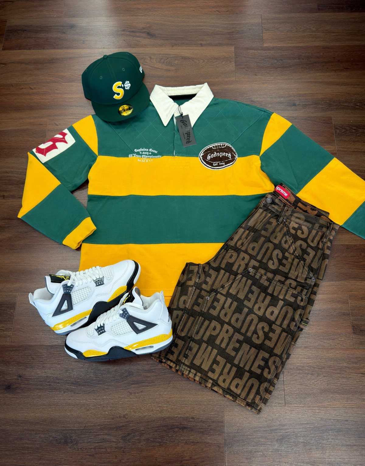 Green and yellow striped shirt, patterned shorts, white sneakers, and a green cap laid on wood.