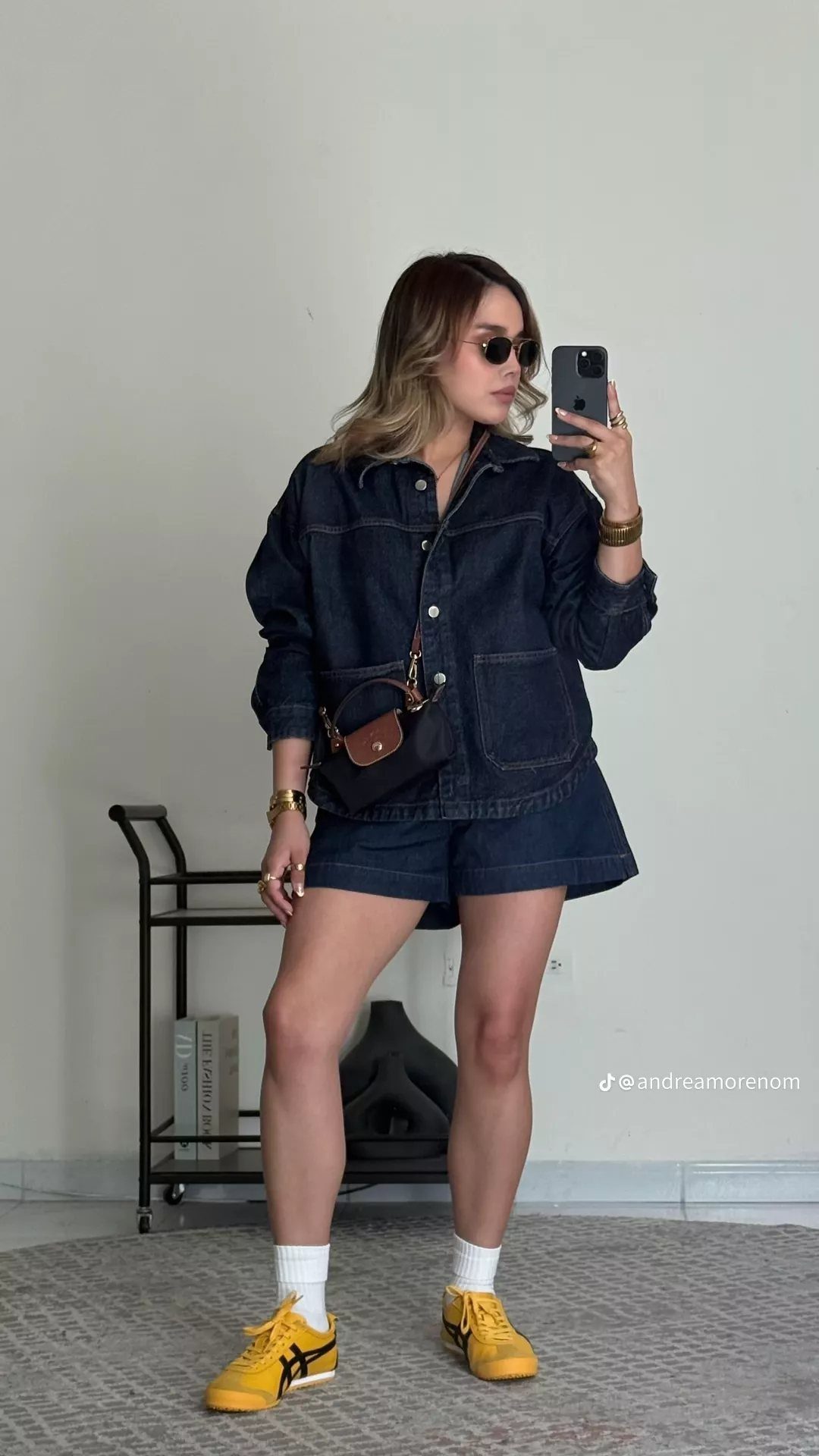 Woman in a denim jacket and shorts wearing bright yellow sneakers.