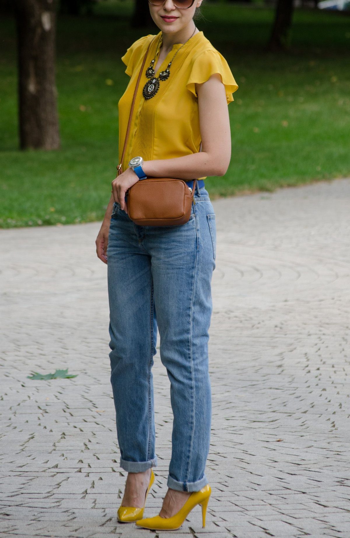 Woman wearing a mustard yellow blouse, blue jeans, and bright yellow high-heeled shoes.